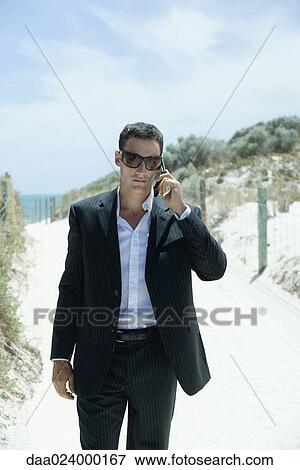 Businessman walking on path through dunes, using cell phone View Large Photo Image Stock Photo - Businessman walking on path through dunes, using cell phone. Fotosearch