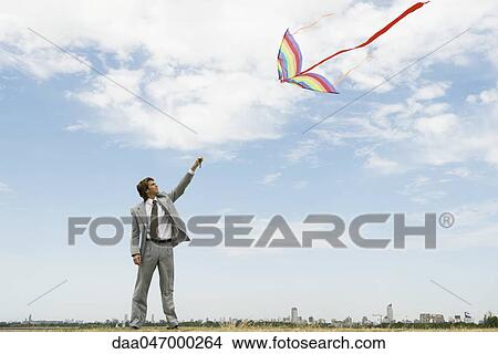 Businessman with arm raised flying kite in field View Large Photo Image Picture - Businessman with arm raised flying kite in field. Fotosearch