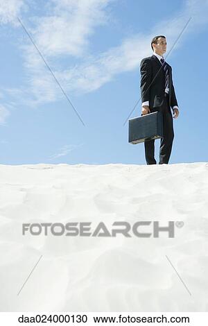 Businessman with briefcase standing on sand, holding briefcase, low angle view View Large Photo Image Stock Image - Businessman with briefcase standing on sand, holding briefcase, low angle view. Fotosearch