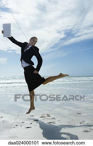 Businesswoman barefoot on beach, jumping into the air with file in hand View Large Photo Image Stock Image - Businesswoman barefoot on beach, jumping into the air with file in hand. Fotosearch