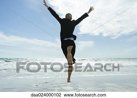 Businesswoman barefoot on beach, jumping into the air, rear view View Large Photo Image Stock Image - Businesswoman barefoot on beach, jumping into the air, rear view. Fotosearch