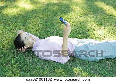 Businesswoman lying in grass, looking at cell phone, smiling View Large Photo Image Stock Image - Businesswoman lying in grass, looking at cell phone, smiling. Fotosearch