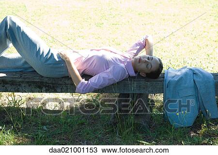 Stock Image - Businesswoman lying on bench, outdoors, eyes closed. Fotosearch