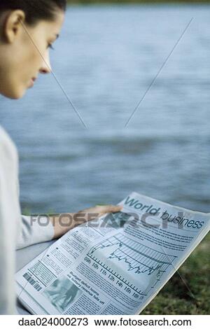 Stock Image - Businesswoman reading newspaper, lake in background. Fotosearch