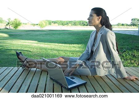 Stock Photo - Businesswoman sitting on deck with laptop. Fotosearch