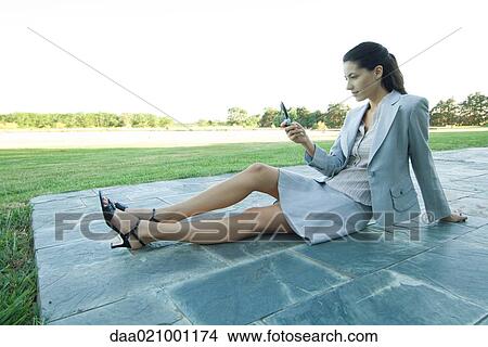 Businesswoman sitting on patio, looking at cell phone View Large Photo Image Picture - Businesswoman sitting on patio, looking at cell phone. Fotosearch