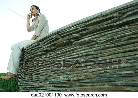 Businesswoman sitting on stone wall, using cell phone, low angle view View Large Photo Image Stock Image - Businesswoman sitting on stone wall, using cell phone, low angle view. Fotosearch