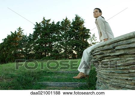 Stock Photo - Businesswoman sitting on stone wall. Fotosearch