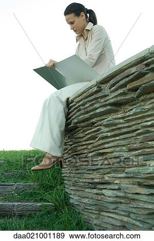 Businesswoman sitting on stone wall, studying file View Large Photo Image Stock Photo - Businesswoman sitting on stone wall, studying file. Fotosearch