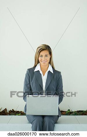 Businesswoman sitting, using laptop computer, smiling at camera View Large Photo Image Stock Image - Businesswoman sitting, using laptop computer, smiling at camera. Fotosearch