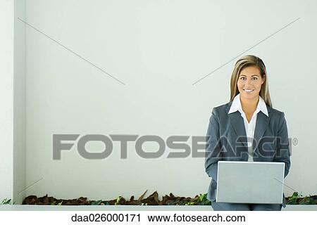 Businesswoman sitting, using laptop computer, smiling at camera View Large Photo Image Stock Image - Businesswoman sitting, using laptop computer, smiling at camera. Fotosearch