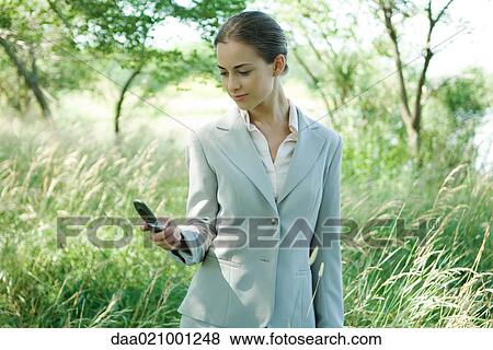 Businesswoman standing in field, looking at cell phone View Large Photo Image Stock Photo - Businesswoman standing in field, looking at cell phone. Fotosearch