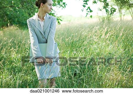 Businesswoman standing in field, holding laptop View Large Photo Image Stock Photograph - Businesswoman standing in field, holding laptop. Fotosearch