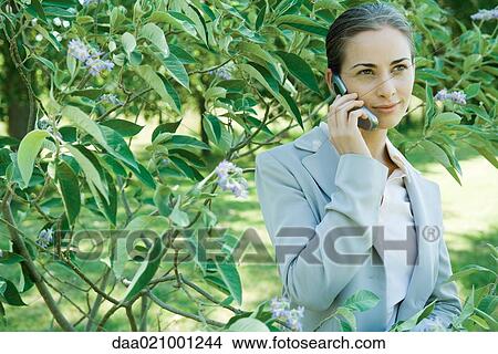 Picture - Businesswoman standing in vegetation, using cell phone. Fotosearch