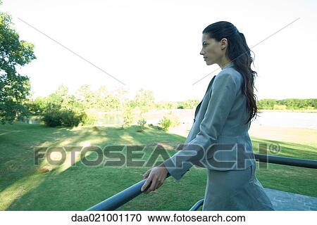 Stock Image - Businesswoman standing outdoors, leaning against rail. Fotosearch