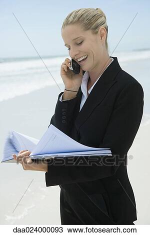 Businesswoman using cell phone and looking at file, standing on beach, smiling View Large Photo Image Stock Image - Businesswoman using cell phone and looking at file, standing on beach, smiling. Fotosearch