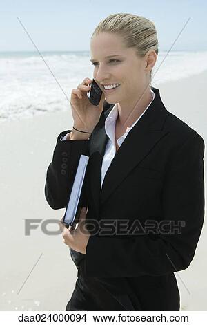 Picture - Businesswoman using cell phone, standing on beach, smiling. Fotosearch