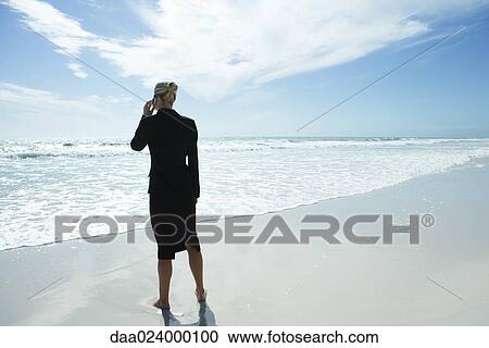 Businesswoman using cell phone, standing on beach, full length, rear view View Large Photo Image Stock Image - Businesswoman using cell phone, standing on beach, full length, rear view. Fotosearch