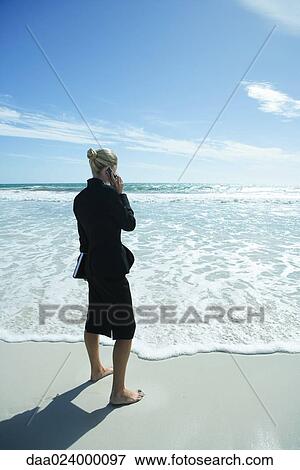 Businesswoman using cell phone, standing on beach barefoot, full length, side view View Large Photo Image Stock Photo - Businesswoman using cell phone, standing on beach barefoot, full length, side view. Fotosearch