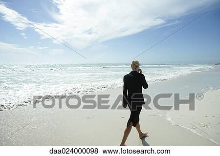 Businesswoman using cell phone, walking barefoot across beach, full length, rear view View Large Photo Image Stock Photo - Businesswoman using cell phone, walking barefoot across beach, full length, rear view. Fotosearch