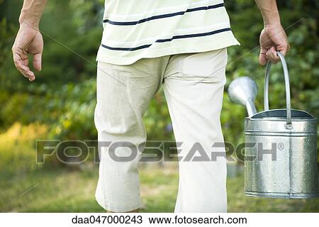 Stock Image - Carrying watering can, rear view. Fotosearch