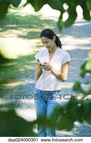 Casually dressed woman holding cell phone, blurred foliage in foreground View Large Photo Image Stock Image - Casually dressed woman holding cell phone, blurred foliage in foreground. Fotosearch