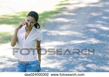 Casually dressed woman using cell phone, smiling as she walks through park View Large Photo Image Stock Image - Casually dressed woman using cell phone, smiling as she walks through park. Fotosearch