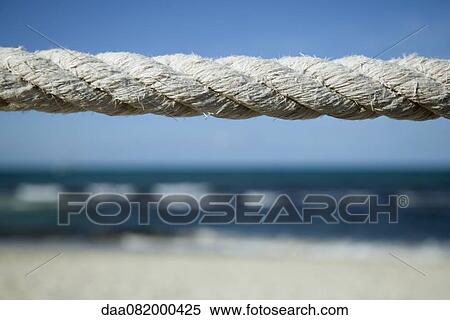 Stock Photography - Close-up of weathered rope with beach in background. Fotosearch