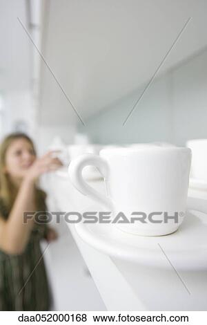 Coffee cup with saucer on shelf, woman in background View Large Photo Image Stock Photo - Coffee cup with saucer on shelf, woman in background. Fotosearch