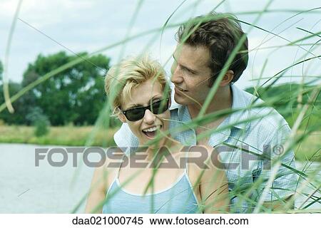 Couple by lake, man whispering to woman, woman laughing View Large Photo Image Stock Photography - Couple by lake, man whispering to woman, woman laughing. Fotosearch