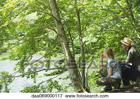 Couple crouching by lake looking at view View Large Photo Image Stock Photo - Couple crouching by lake looking at view. Fotosearch