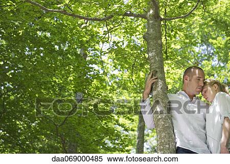 Stock Photography - Couple embracing by tree. Fotosearch