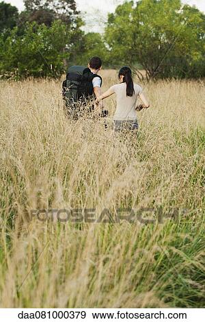 Stock Photo - Couple hiking in field, rear view. Fotosearch
