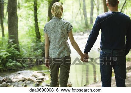 Stock Photograph - Couple holding hands, looking at stream running through woods. Fotosearch