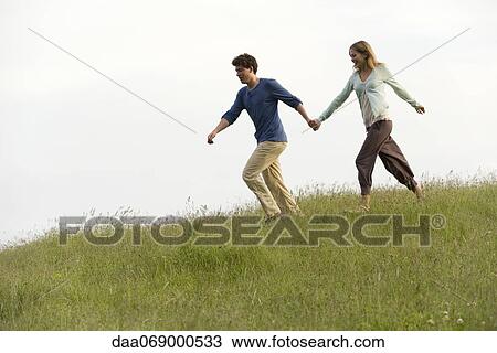 Couple holding hands running on meadow View Large Photo Image Stock Image - Couple holding hands running on meadow. Fotosearch