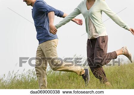Couple holding hands running on meadow, cropped View Large Photo Image Stock Photo - Couple holding hands running on meadow, cropped. Fotosearch