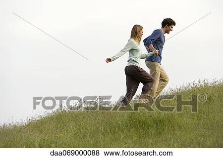 Couple holding hands walking on meadow View Large Photo Image Stock Photo - Couple holding hands walking on meadow. Fotosearch