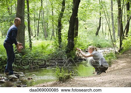 Stock Photography - Couple in woods, woman splashing water at man. Fotosearch