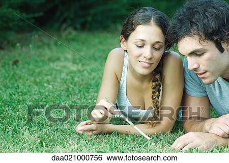 Couple lying in grass, woman holding twig View Large Photo Image Stock Photograph - Couple lying in grass, woman holding twig. Fotosearch