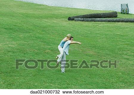 Stock Image - Couple on lawn, man holding woman piggyback, pointing to distance. Fotosearch