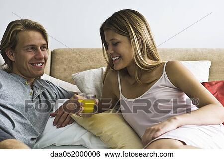 Couple reclining together in bed, woman holding glass of juice View Large Photo Image Stock Photograph - Couple reclining together in bed, woman holding glass of juice. Fotosearch