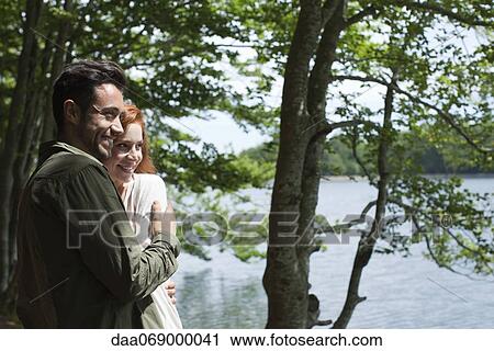 Stock Image - Couple relaxing together beside lake. Fotosearch