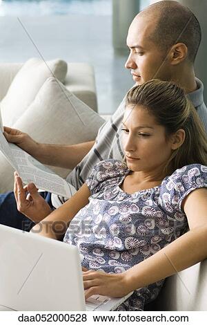 Couple relaxing together on sofa, man reading and woman using laptop computer View Large Photo Image Stock Photo - Couple relaxing together on sofa, man reading and woman using laptop computer. Fotosearch
