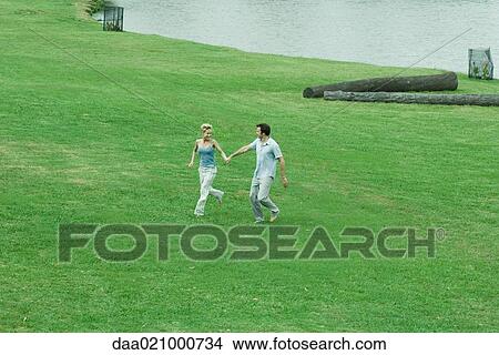Picture - Couple running across grass, hand in hand, full length, high angle view. Fotosearch