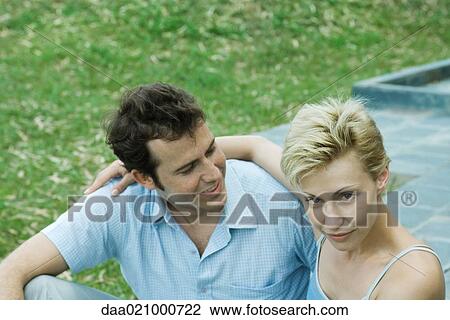 Stock Image - Couple sitting in backyard, man looking at woman, woman looking at camera. Fotosearch