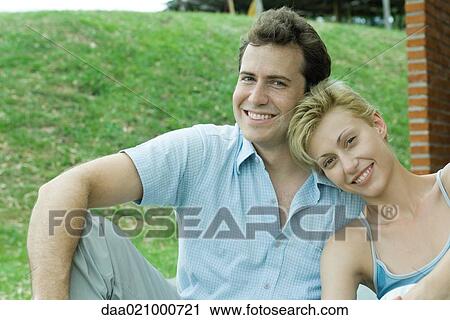 Stock Image - Couple sitting in backyard smiling at camera, close-up. Fotosearch