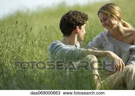 Couple sitting in grass, looking at each other affectionately View Large Photo Image Stock Image - Couple sitting in grass, looking at each other affectionately. Fotosearch