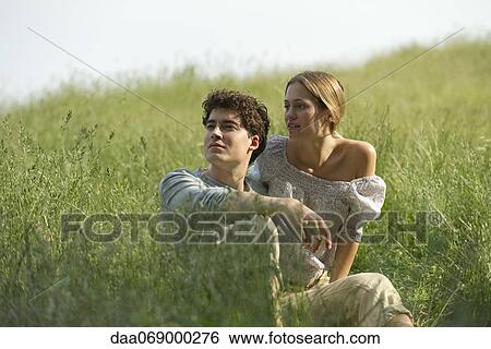 Stock Photograph - Couple sitting in tall grass looking into distance. Fotosearch