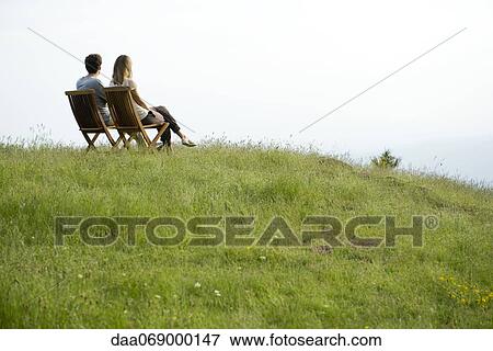 Couple sitting on chairs on top of hill looking at view View Large Photo Image Stock Photo - Couple sitting on chairs on top of hill looking at view. Fotosearch
