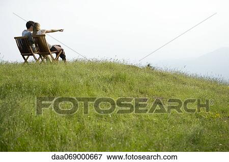Couple sitting on chairs on top of hill looking at view, woman pointing toward distance View Large Photo Image Stock Photo - Couple sitting on chairs on top of hill looking at view, woman pointing toward distance. Fotosearch